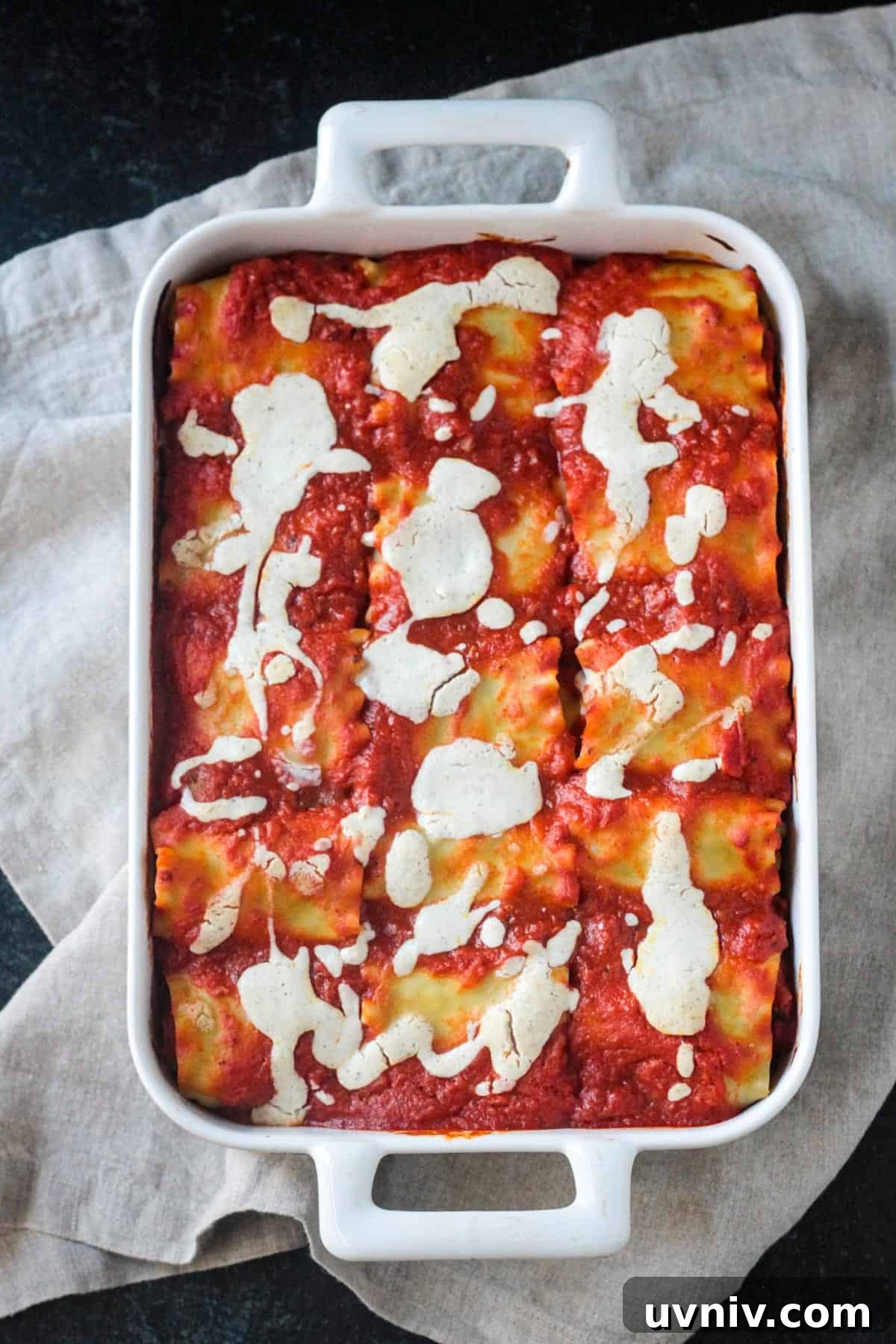 Full pan of lasagna roll ups covered in marinara and drizzled with white sauce.