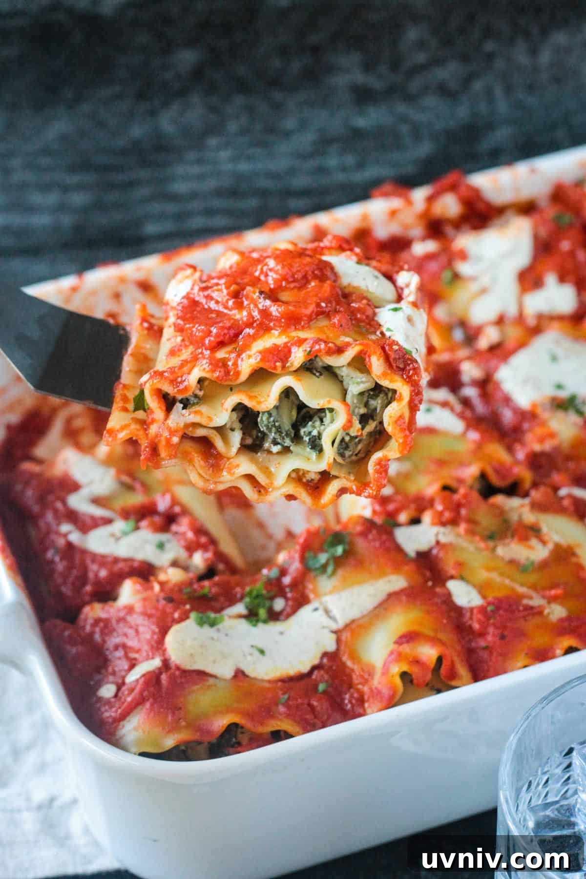 Spatula lifting one spinach pasta roll out of a baking dish.