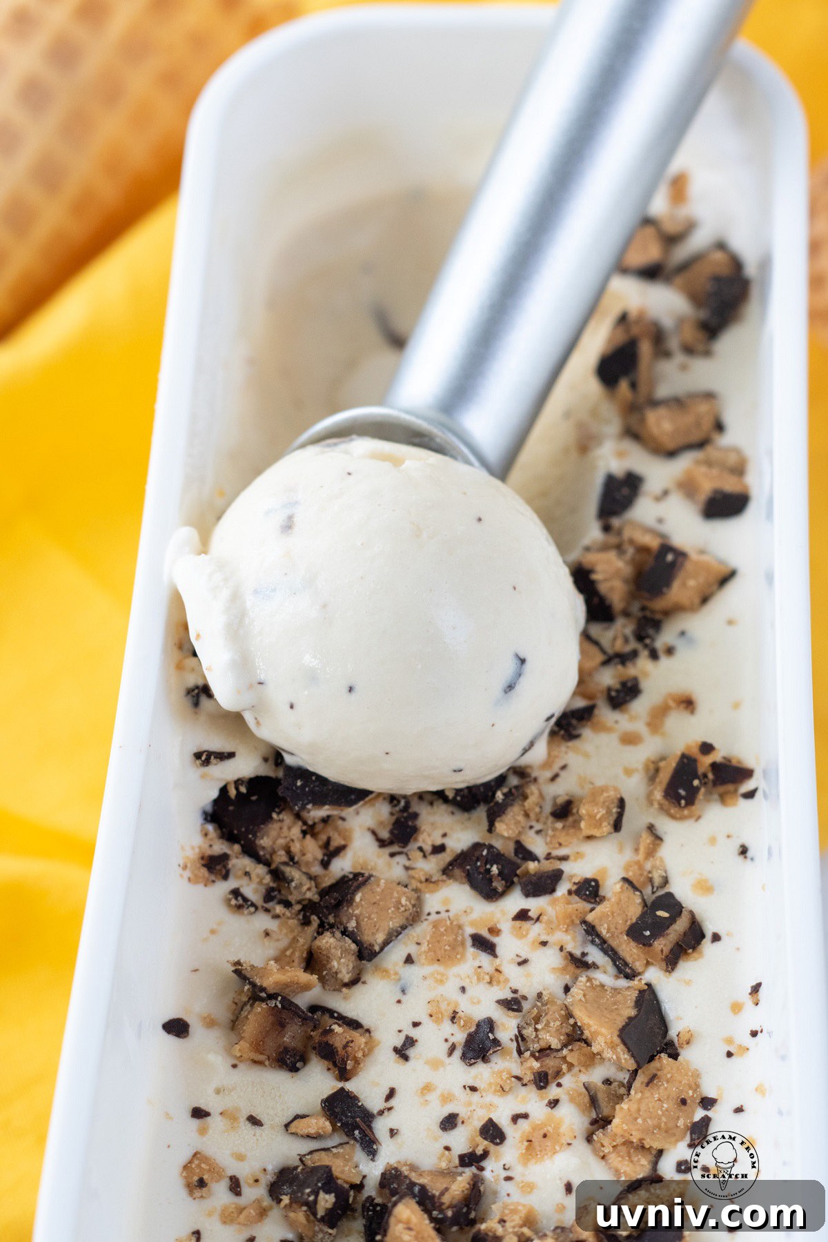 a metal ice cream scoop pulling through a rectangular ice cream container of butter brickle.