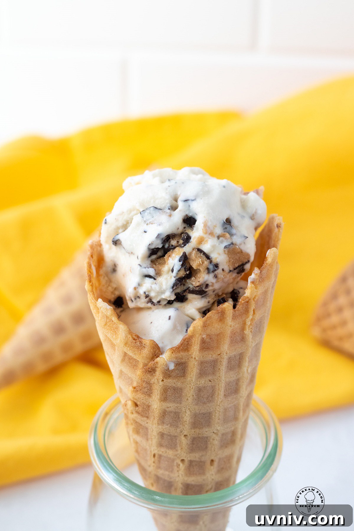 a waffle cone holding homemade ice cream with butter brickle toffee pieces. in the background is a yellow cloth.