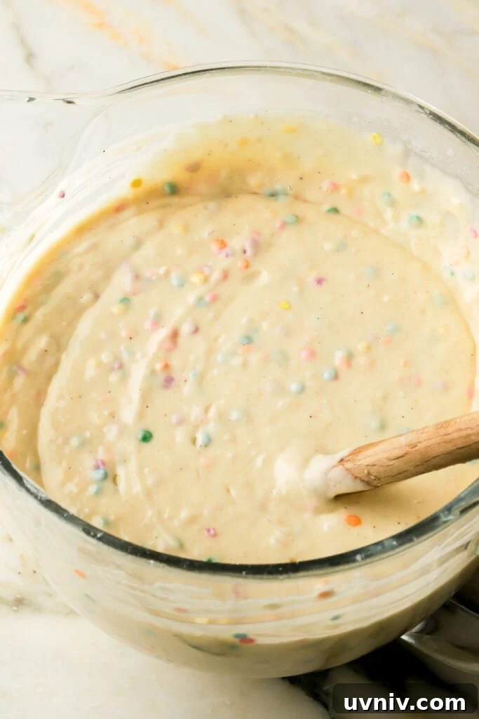 Party-Size Vanilla Birthday Sheet Cake Recipe 10 vanilla cake batter with sprinkles mixed into it, in glass mixing bowl with spatula