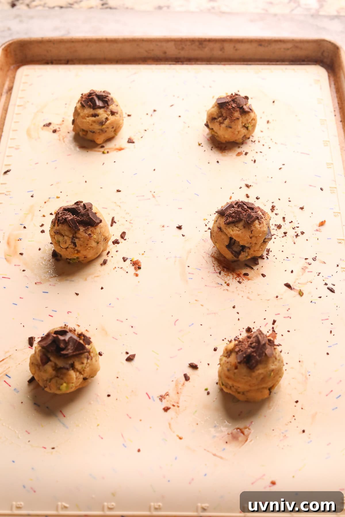 Brown Butter Pistachio Chocolate Chip Cookies Recipe 8 Brown butter pistachio chocolate chip cookie dough balls on a baking sheet before going in the oven.