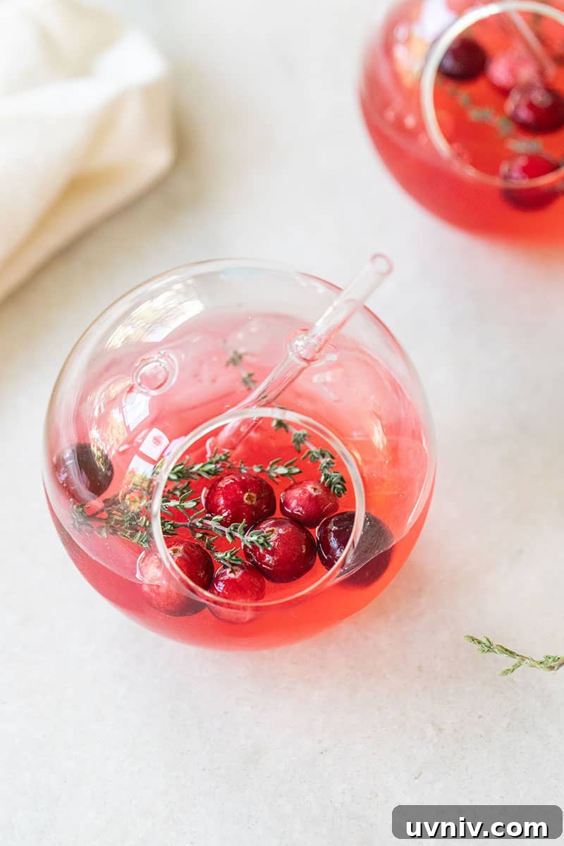 Cranberry and Thyme Gin & Tonic Recipe for Holiday Cocktails 2 Cranberry and Thyme gin and tonic in a round clear glass ball.