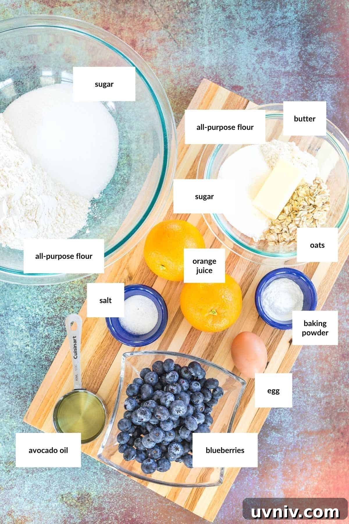 Moist Blueberry Orange Muffins with Zesty Citrus Glaze 3 Overhead view of labeled baking ingredients for Blueberry Orange Muffins, including flour, sugar, butter, oats, orange juice, salt, baking powder, egg, avocado oil, and blueberries on a colorful surface.