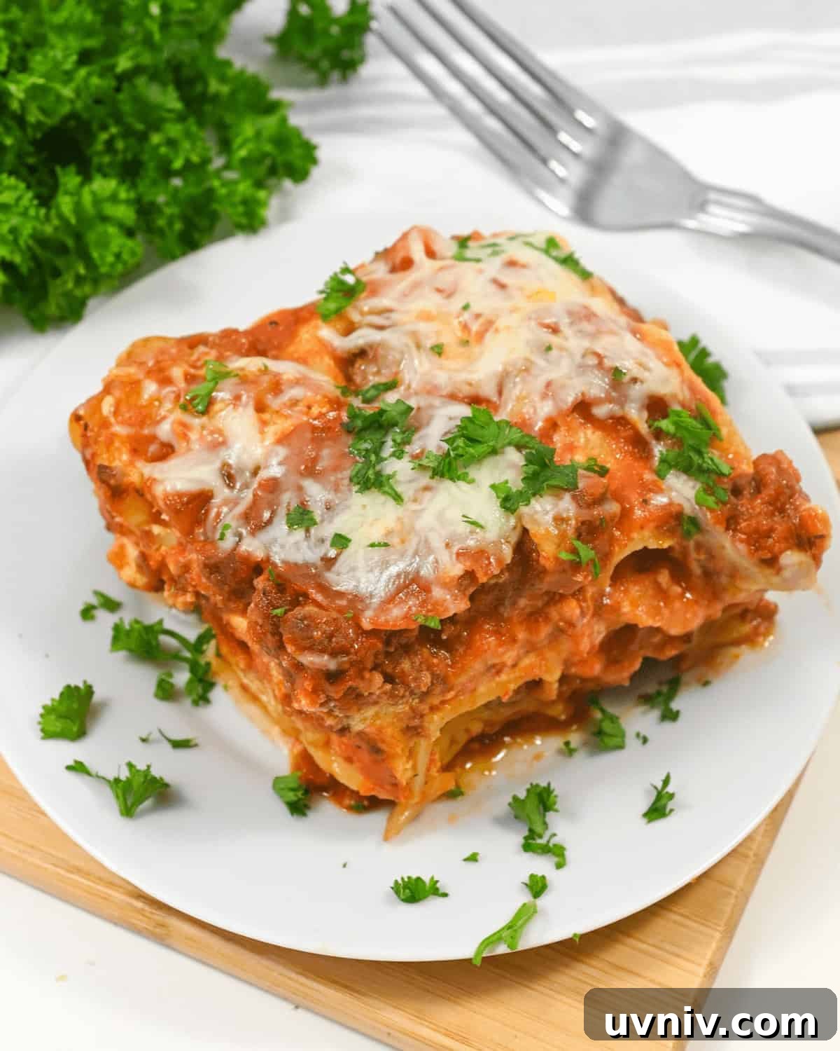 Slow Cooker No-Fuss Lasagna: Cheesy One-Pot Recipe 8 A slice of lazy lasagna topped with melted cheese and parsley, served on a square white plate with a wooden table background.