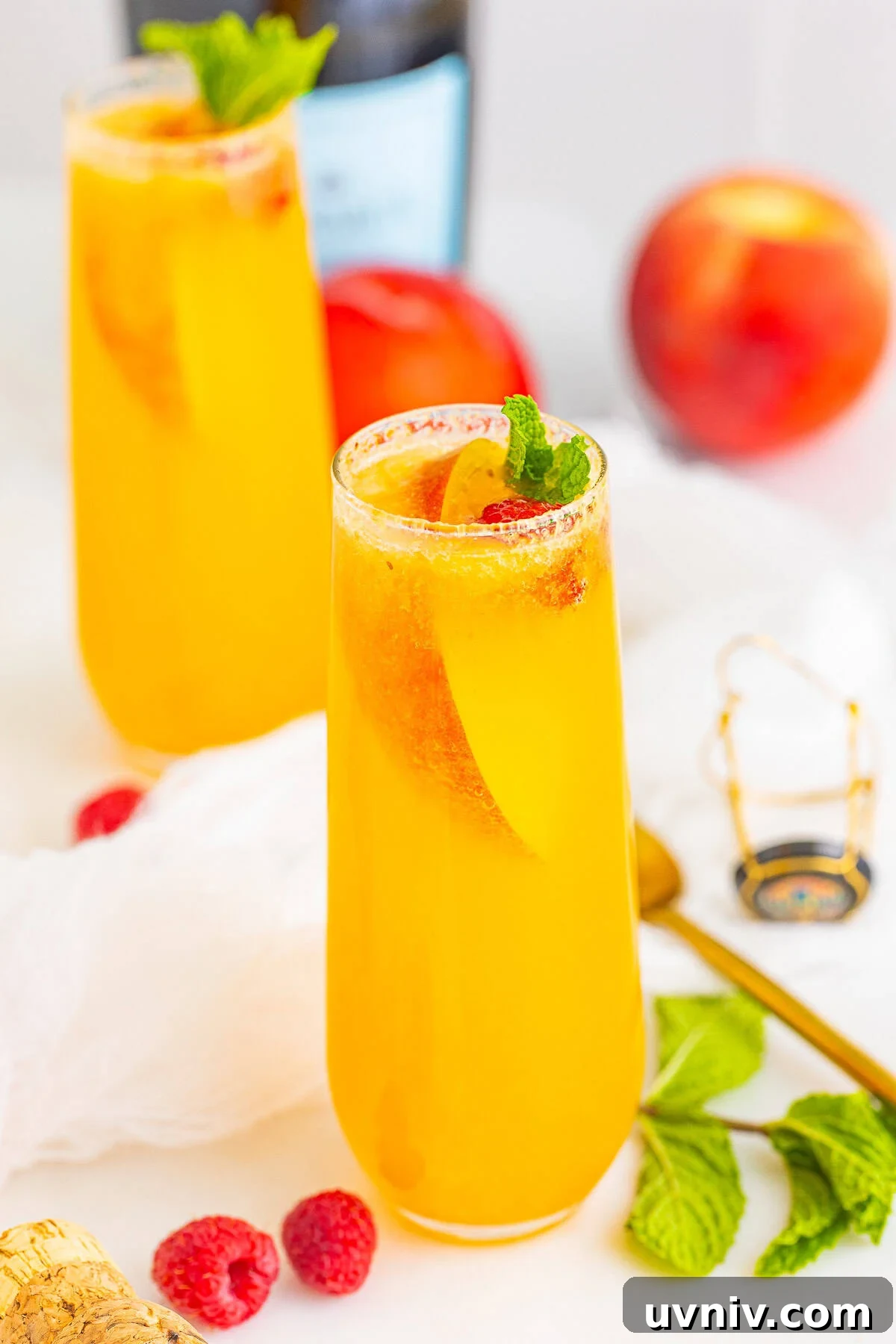 Two peach bellini cocktails in champagne flutes garnished with peach slices, raspberries, and mint.