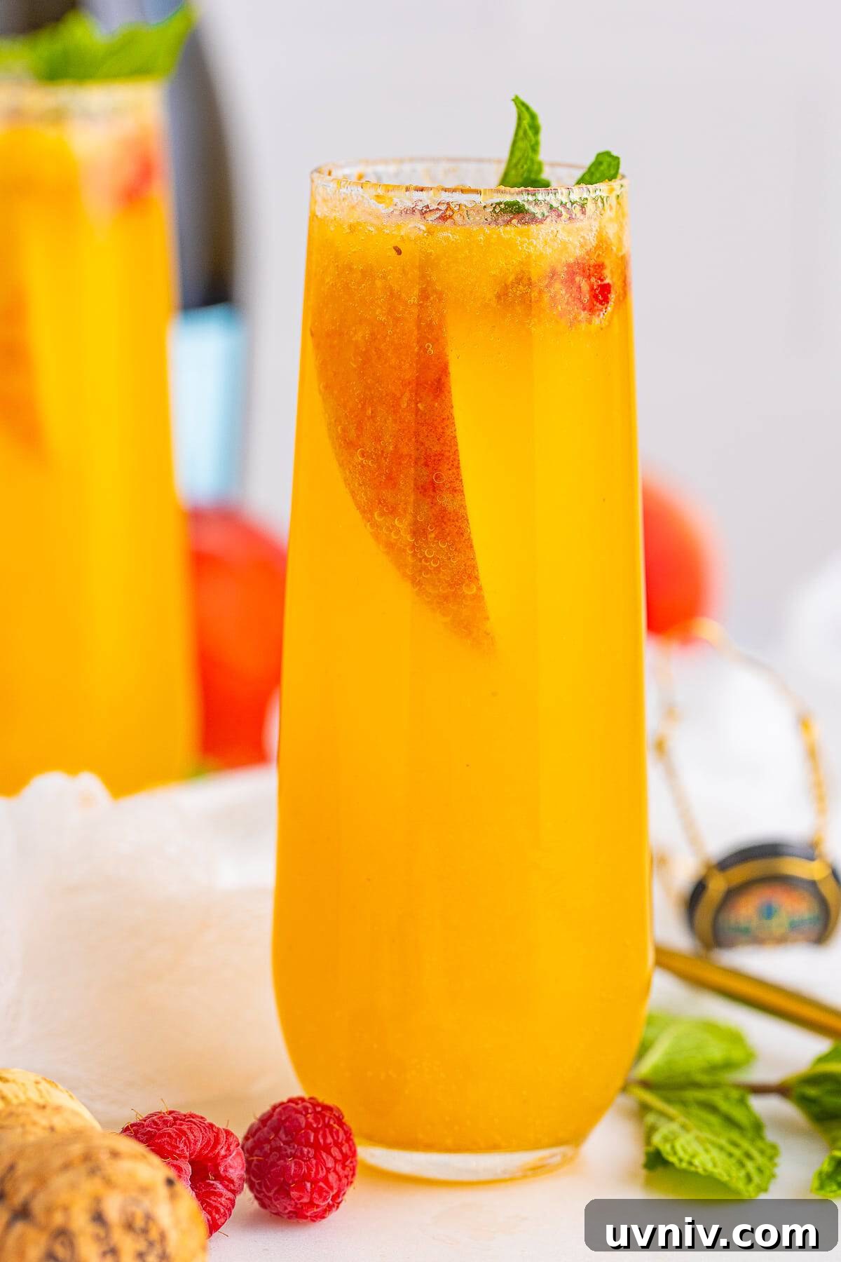 A close up of a peach bellini cocktail in a flute garnished with a fresh peach slice and mint.
