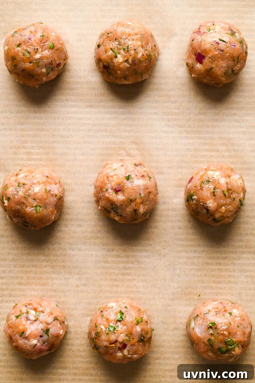 How to make Greek chicken meatballs: Meatballs evenly spaced on a parchment lined baking sheet before cooking.