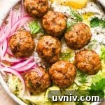 Baked Greek chicken meatballs in a shallow bowl with rice, cabbage salad, thinly sliced pickled red onions, creamy dairy free tzatziki sauce, and a lemon wedge. Bowl is garnished with scattered fresh dill and parsley, black pepper, and a tiny bit of aleppo chili flakes.
