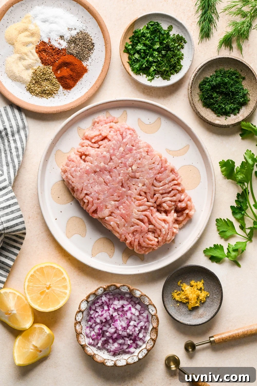 Ingredients for making Greek chicken meatballs in various ceramics, on a cream colored background with a striped linen and sprigs of fresh dill and parsley peeking into the frame. 