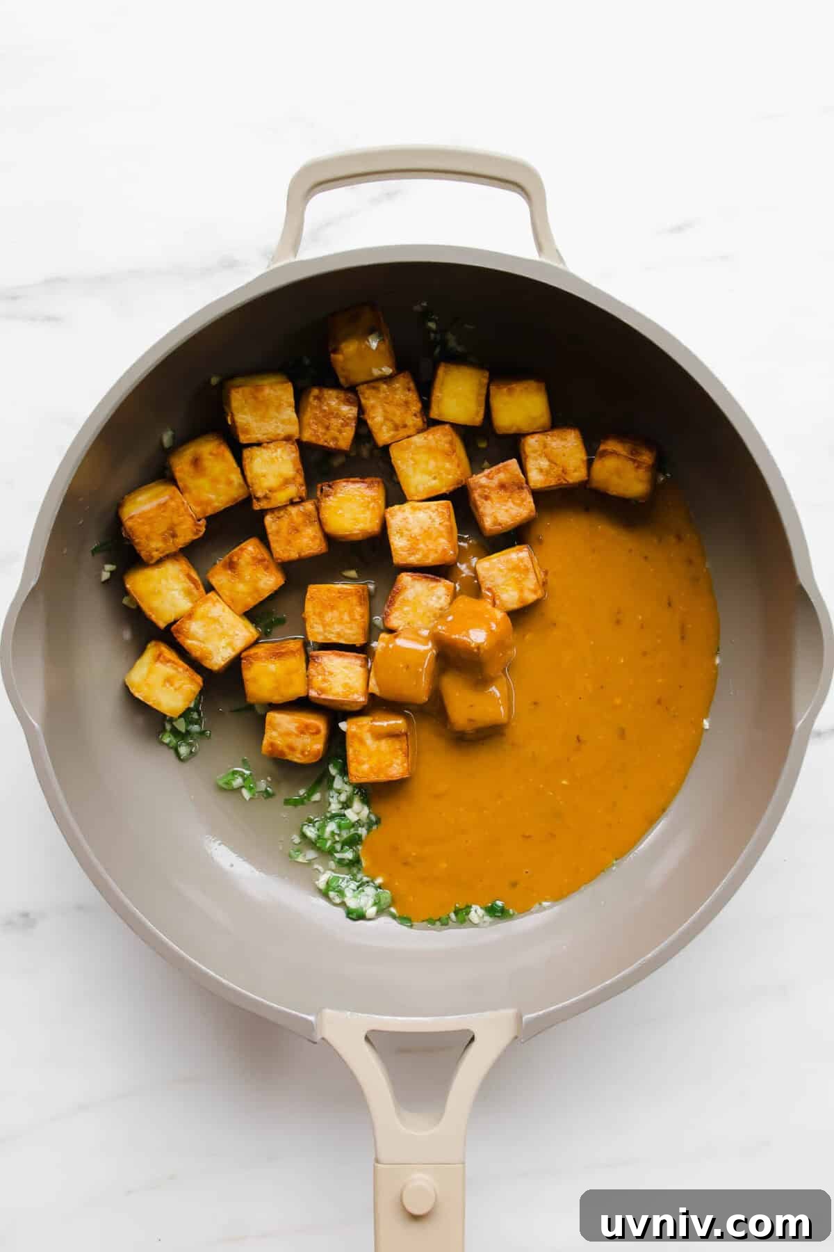 Crispy Baked Peanut Butter Tofu with Sticky Soy Glaze 7 tofu cubes, chopped garlic and scallions and tofu in a taupe pan.