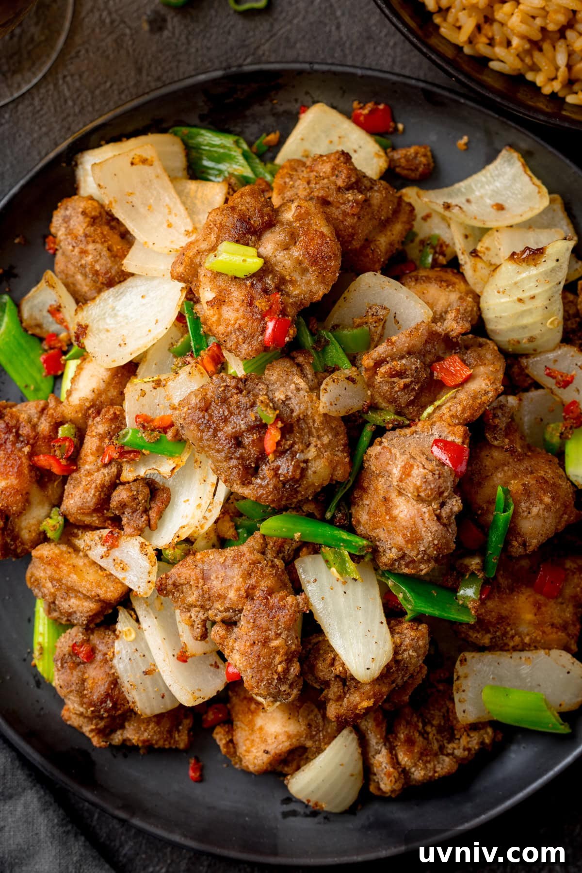 Crispy Salt and Pepper Chicken Made in the Air Fryer 2 Overhead close up image of a dark plate filled with Air Fryer Chicken with onions, spring onions, and red chillies.