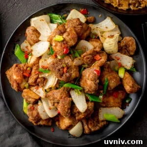 Crispy Salt and Pepper Chicken Made in the Air Fryer 6 A plate of Salt and Pepper Chicken pieces with onions, chillies, and spring onions on a dark plate.
