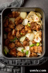 Crispy Salt and Pepper Chicken Made in the Air Fryer 7 Salt and Pepper Chicken pieces with chopped onion, scallions and chillies in an air fryer basket, seen from above.