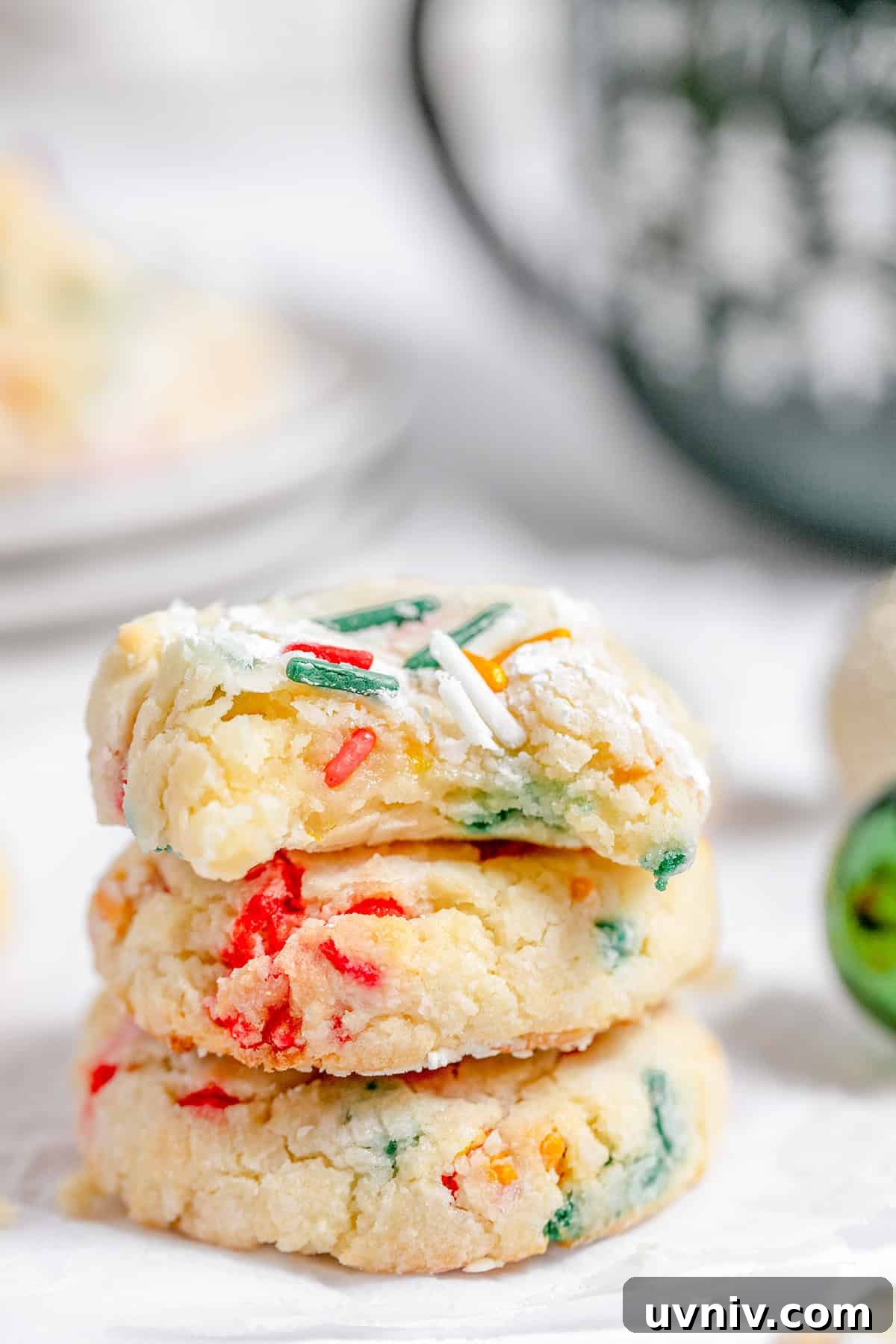 A stack of three gooey butter cookies, adorned with colorful sprinkles, rests on a white surface against a softly blurred background.