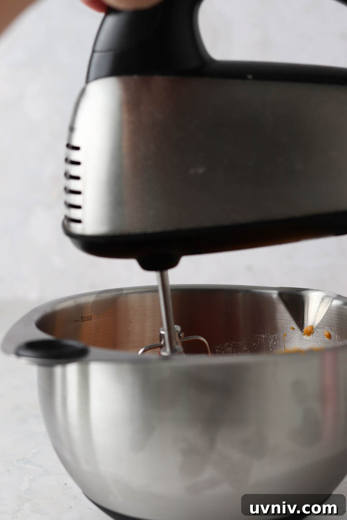 Hand mixer in a metal mixing bowl filled with sweet potatoes.