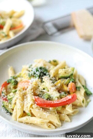 Creamy vegetable pasta in a white bowl with parmesan cheese in background.