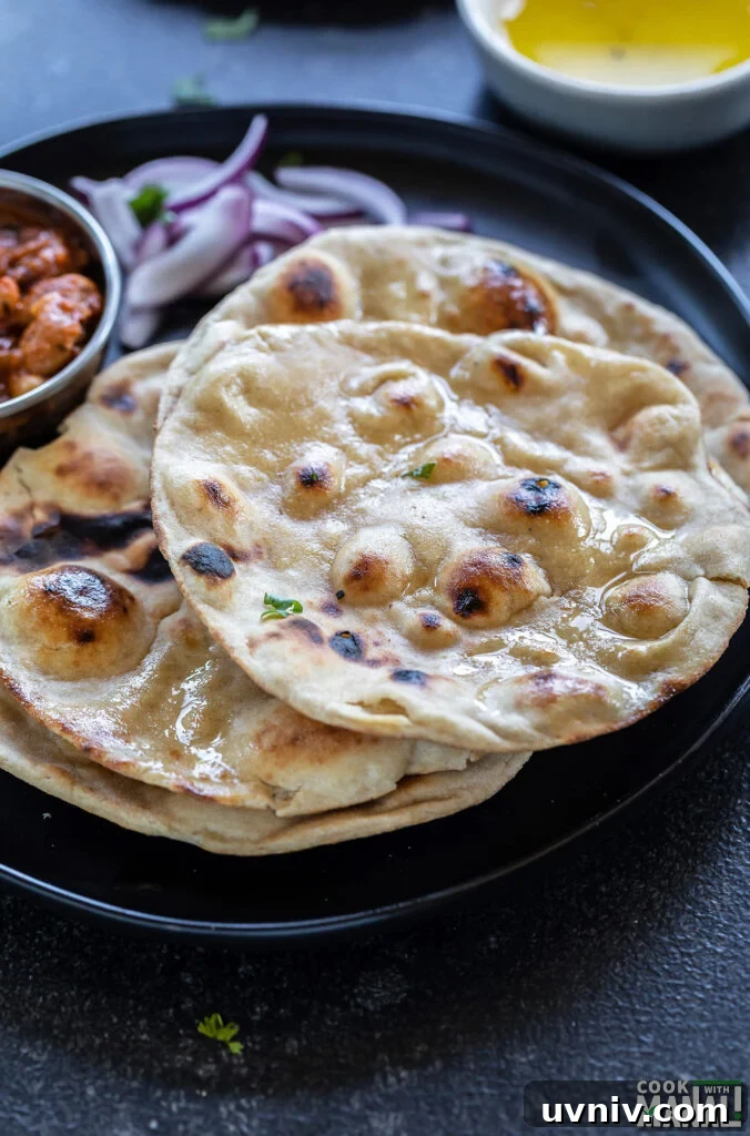 How to Make Authentic Tandoori Roti at Home 7 rotis arranged on a plate with a bowl of creamy curry and another bowl of ghee in the background