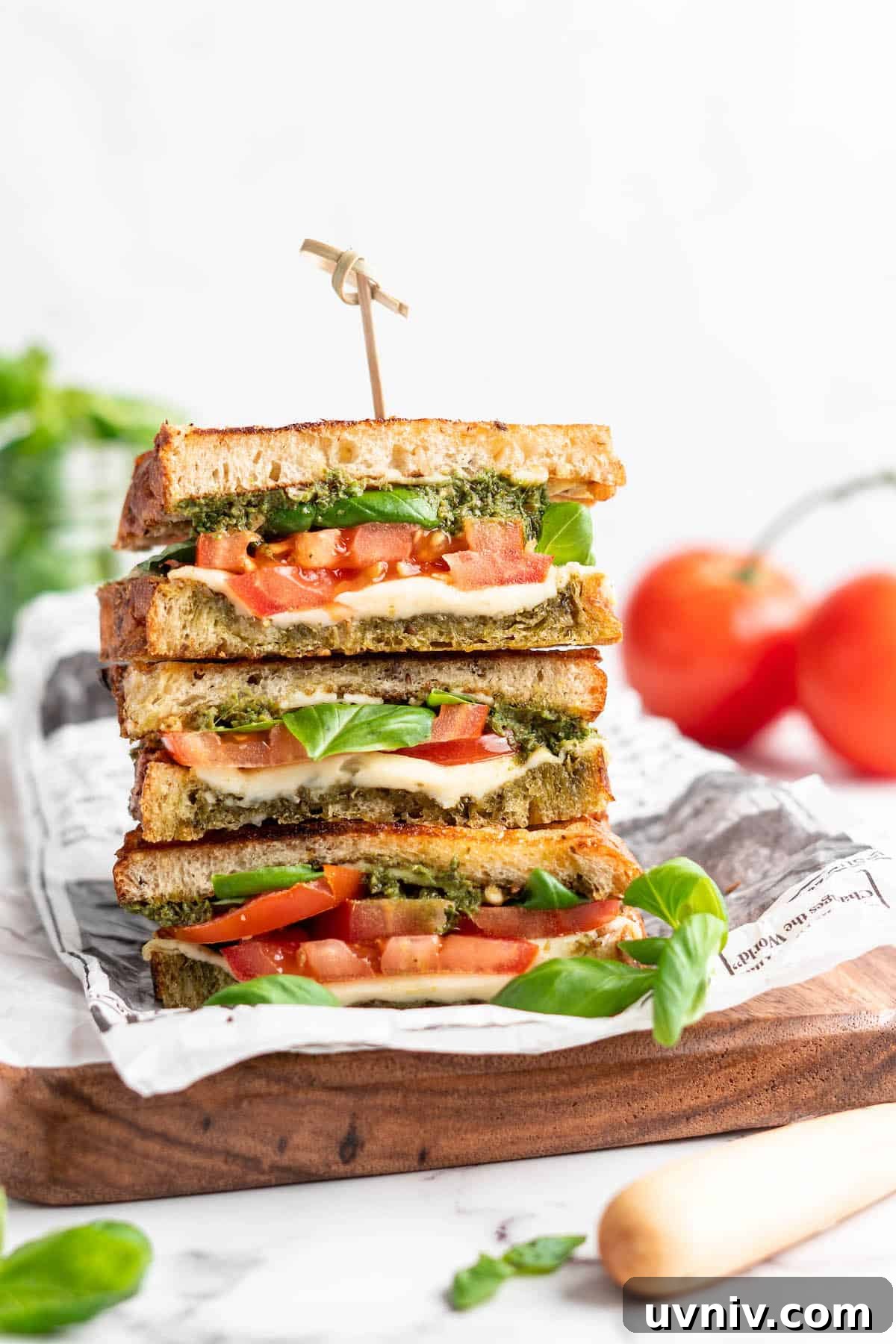This vegan Caprese sandwich layers plant-based mozzarella with fresh tomatoes and parsley pesto, all on crusty French bread. Best lunch ever! Three stacked vegan caprese sandwiches set on wooden cutting board