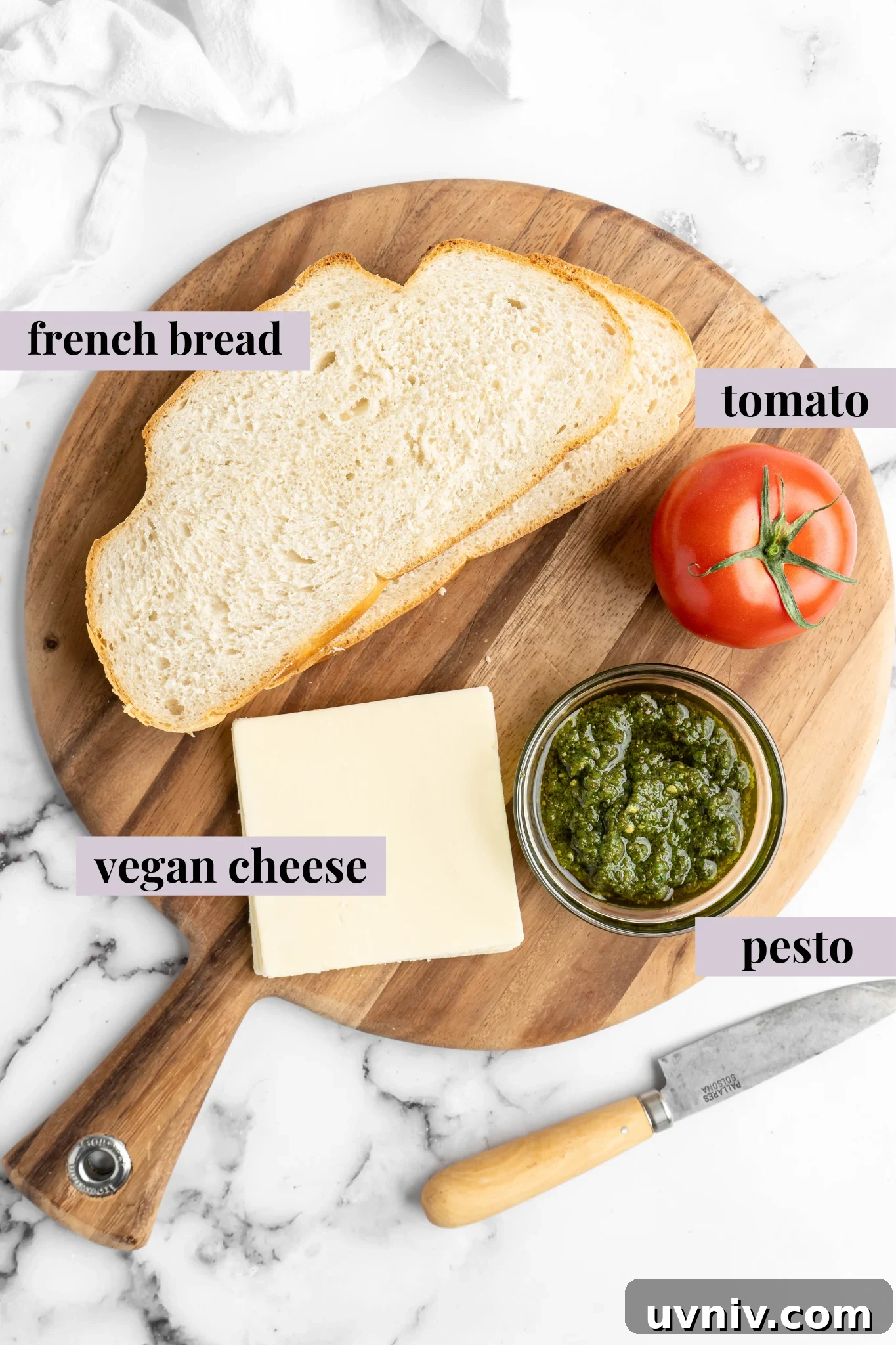This vegan Caprese sandwich layers plant-based mozzarella with fresh tomatoes and parsley pesto, all on crusty French bread. Best lunch ever! Overhead view of vegan caprese sandwich ingredients with labels