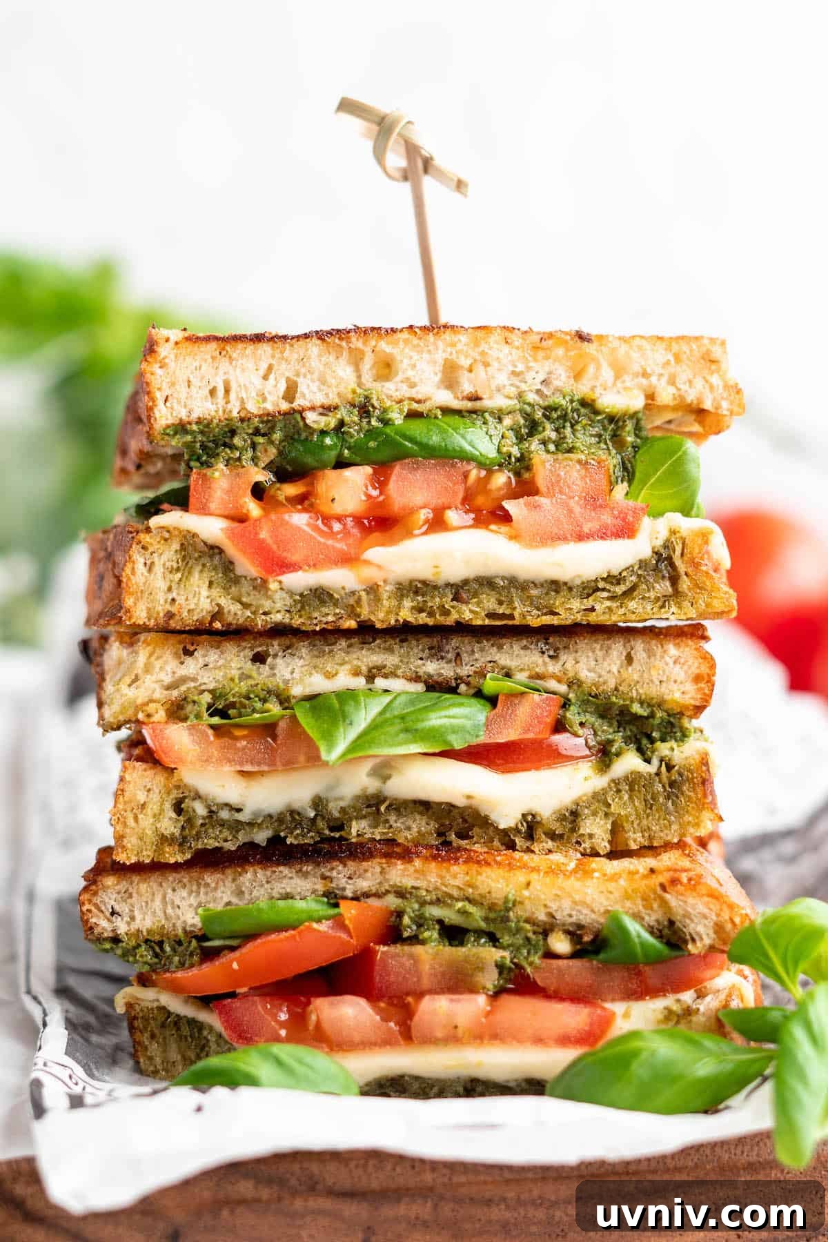 This vegan Caprese sandwich layers plant-based mozzarella with fresh tomatoes and parsley pesto, all on crusty French bread. Best lunch ever! Three stacked vegan caprese sandwiches, cut to show layers of ingredients inside
