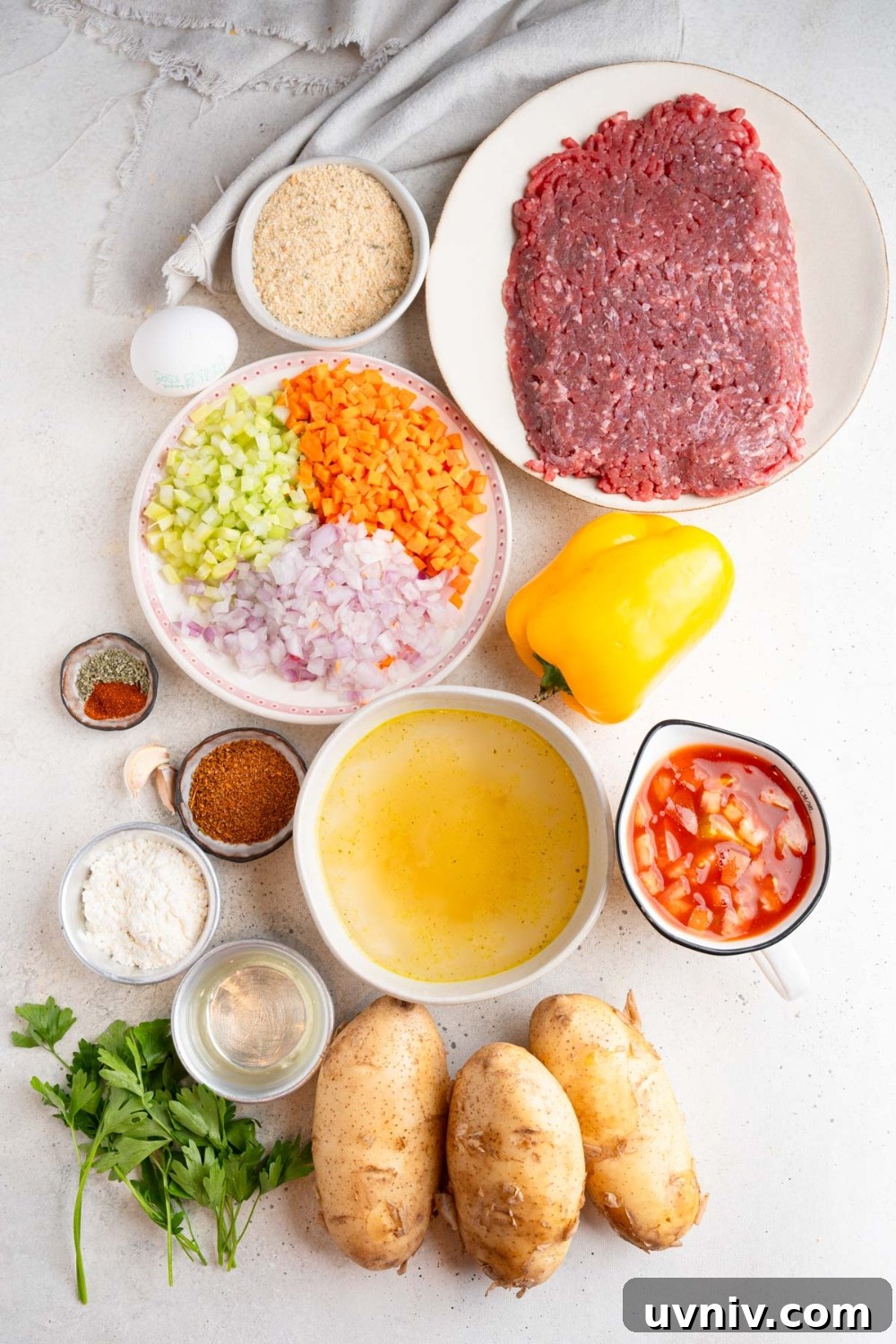 An overhead shot of several bowls in various sizes containing ingredients to make cajun meatball stew including raw beef, diced vegetables, potatoes, yellow pepper, diced tomatoes, and seasonings.