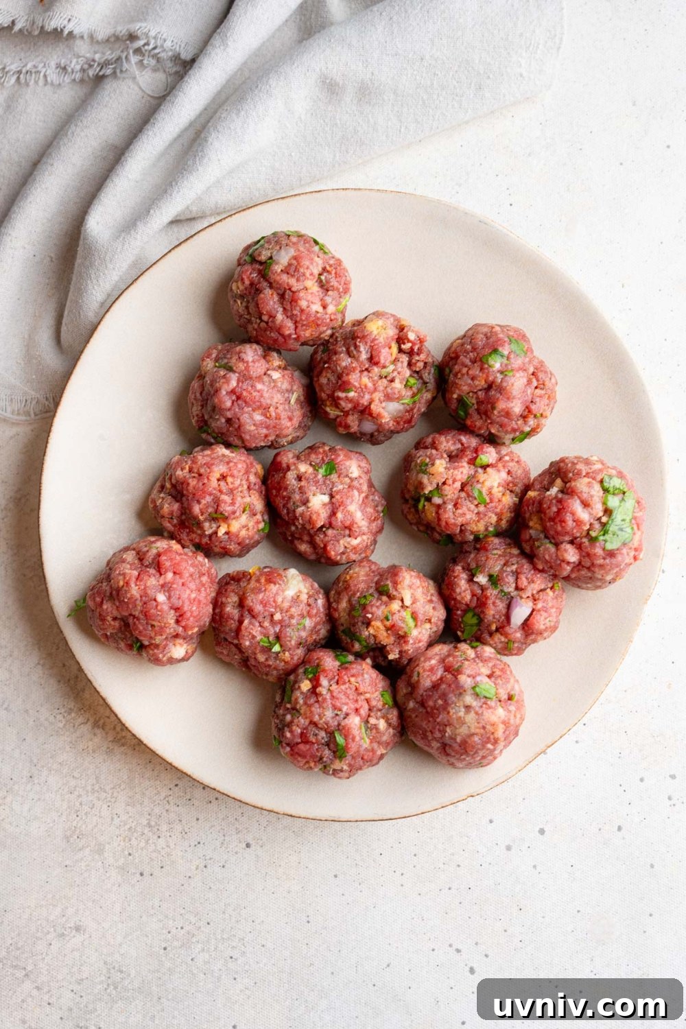A ceramic plate with several uncooked cajun meatballs. The plate is on a white counter with a white cloth napkin.