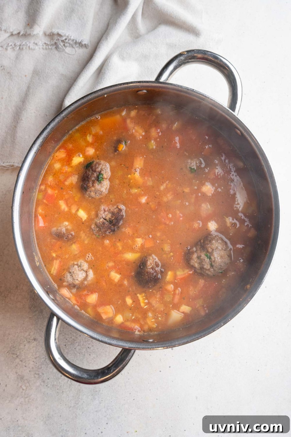 A large stainless steel pot with simmering cajun meatball stew. The pot is on a white counter with a white cloth napkin.