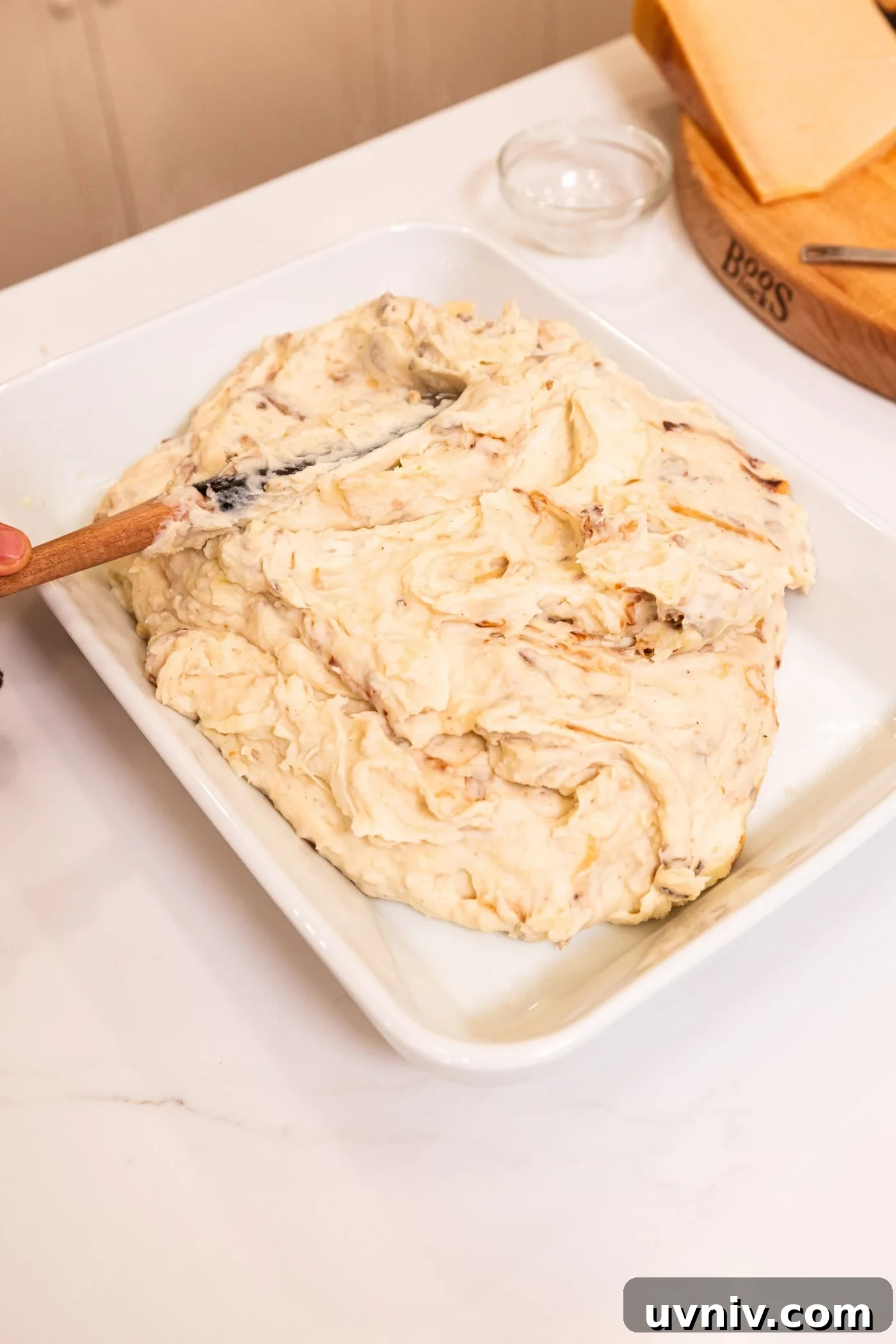 French Onion Potato Casserole Recipe with Melty Cheese 14 Large white baking dish filled with French onion potato mixture with offset spatula smoothing it out to an even layer.
