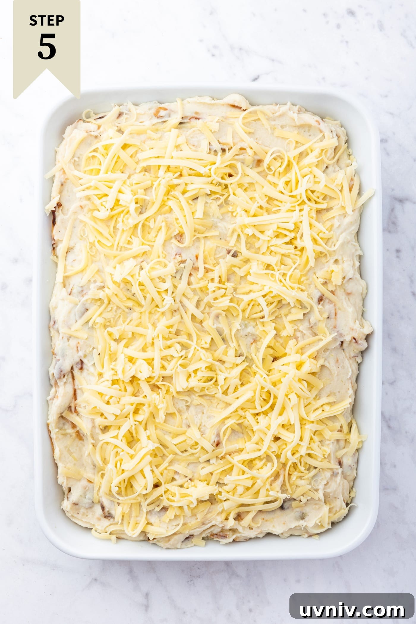 French Onion Potato Casserole Recipe with Melty Cheese 15 White marble surface with white baking dish filled with unbaked French onion potato casserole