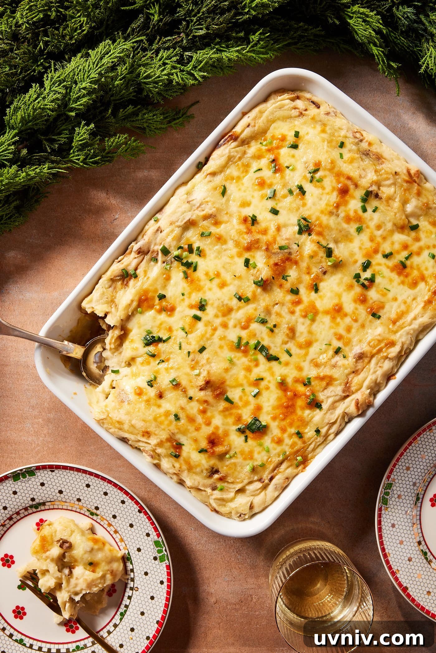French Onion Potato Casserole Recipe with Melty Cheese 3 White baking dish filled with potato casserole with cheese melted on top sprinkled with parsley with serving on a Christmas plate with garland.