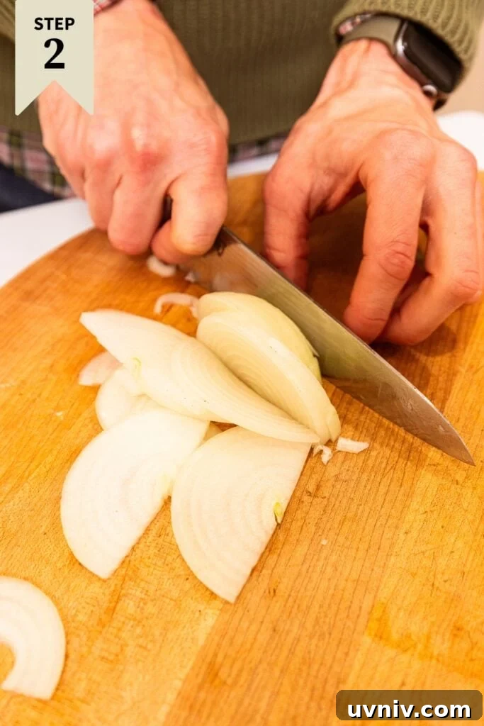 French Onion Potato Casserole Recipe with Melty Cheese 7 Two hands slicing onion into thin strips on wood cutting board with knife.