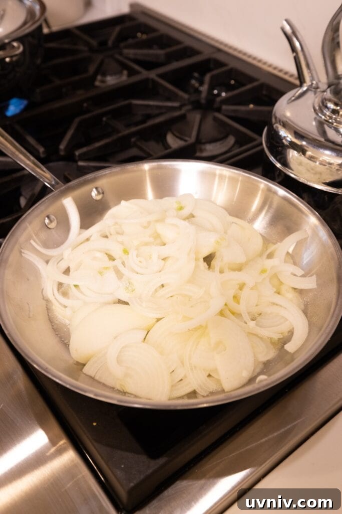 French Onion Potato Casserole Recipe with Melty Cheese 8 Slices of onion in a metal skillet at the beginning of caramelization process.