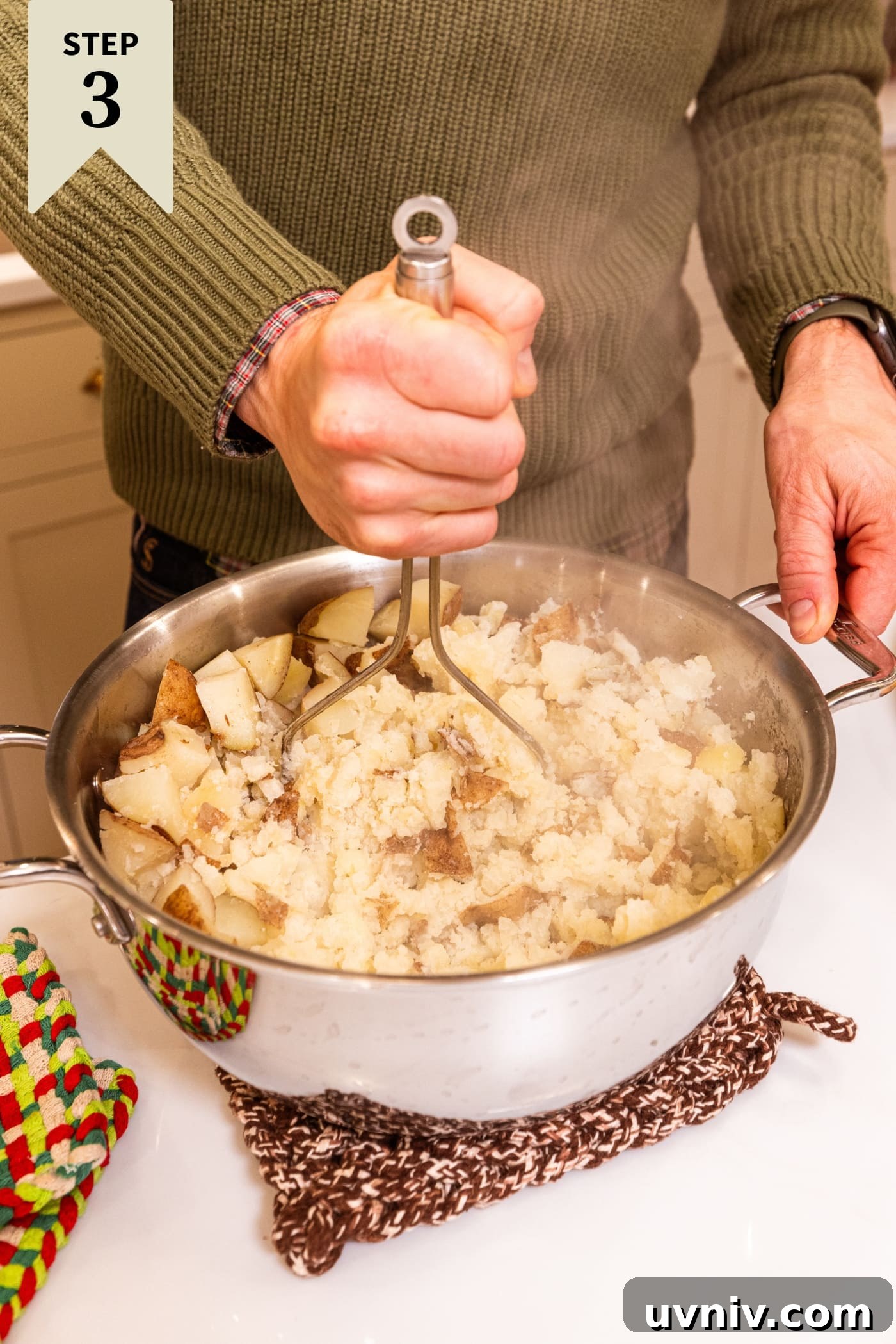 French Onion Potato Casserole Recipe with Melty Cheese 9 Hand holding potato masher mashing potatoes together in a large stockpot.