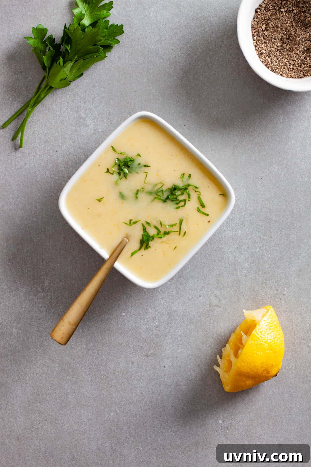 Zesty Preserved Lemon Vinaigrette Recipe for Salads & Marinades 7 Chopped parsley and black pepper sprinkled on top of a preserved lemon vinaigrette in a small white bowl on a gray table.