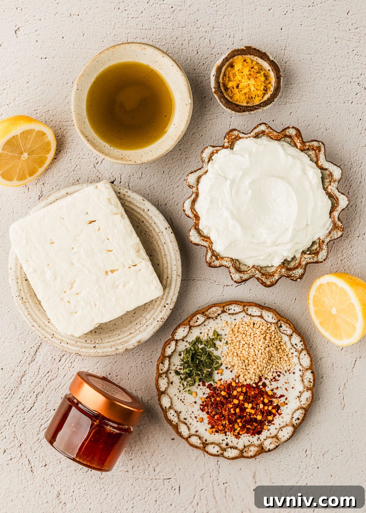 Whipped Feta with Honey in 5 Minutes — Creamy Dip Recipe 3 White and brown bowls of feta, yogurt, oil, lemon zest, sesame seeds, and pepper flakes on a tan counter next to a jar of honey.