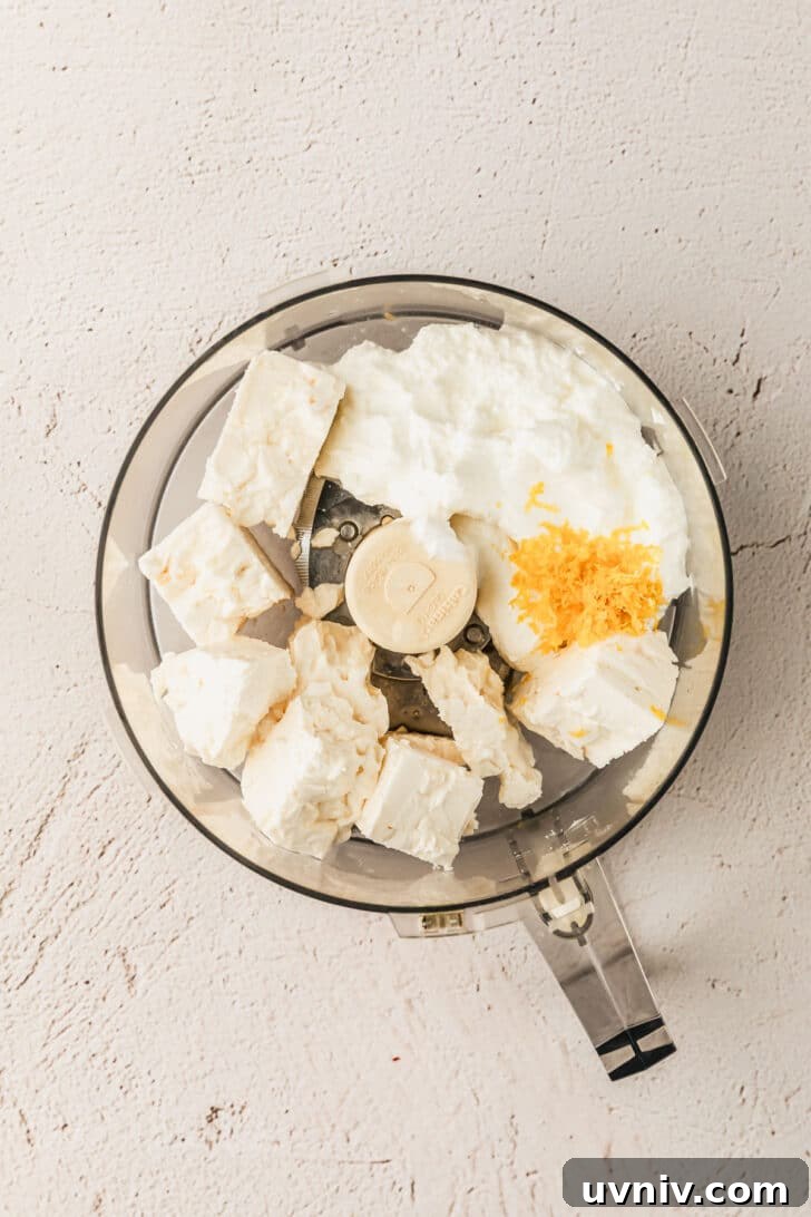 Whipped Feta with Honey in 5 Minutes — Creamy Dip Recipe 4 A food processor with cheese, yogurt, and lemon zest on a tan counter.