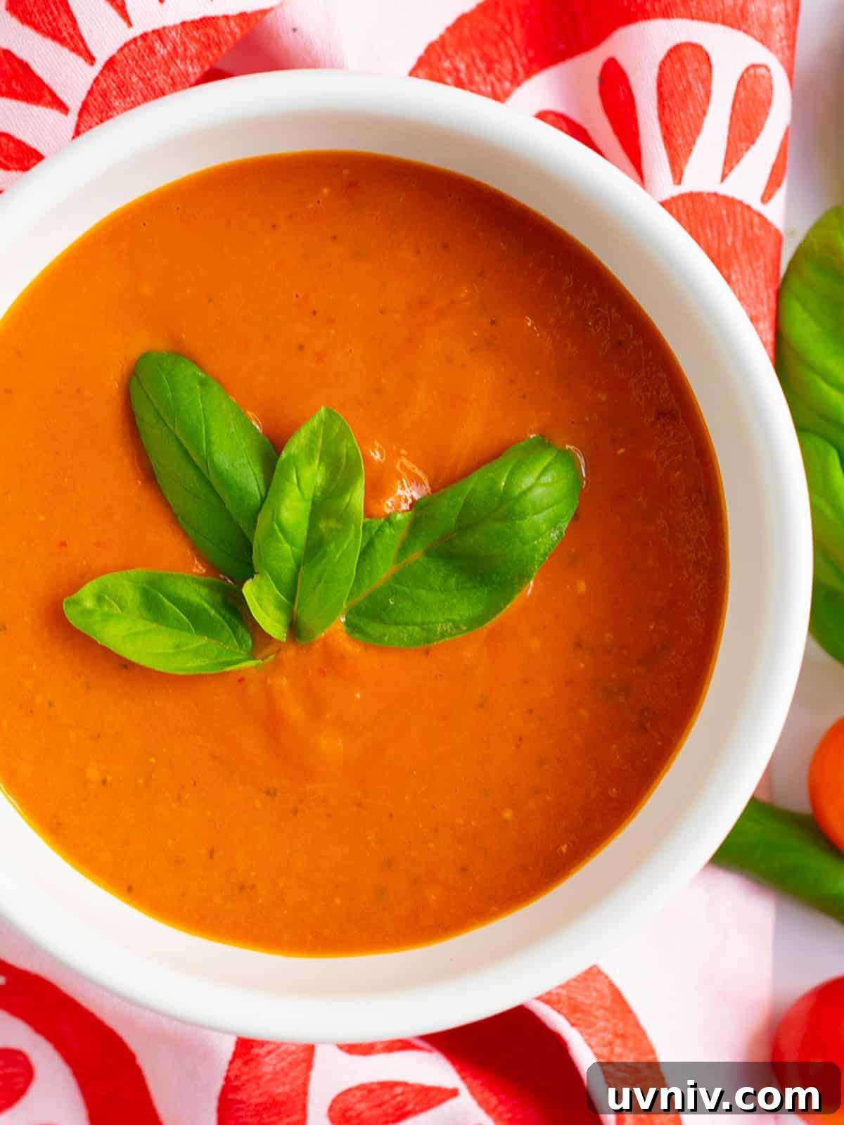 Roasted Tomato Sauce Recipe — Rich Flavor in Minutes 2 Close up of roasted tomato pasta sauce in a white bowl with fresh basil on top and tomato print linen in the background.