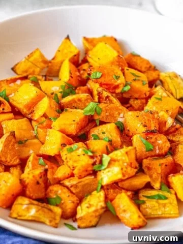 Cubed butternut squash in a white bowl topped with parsley.