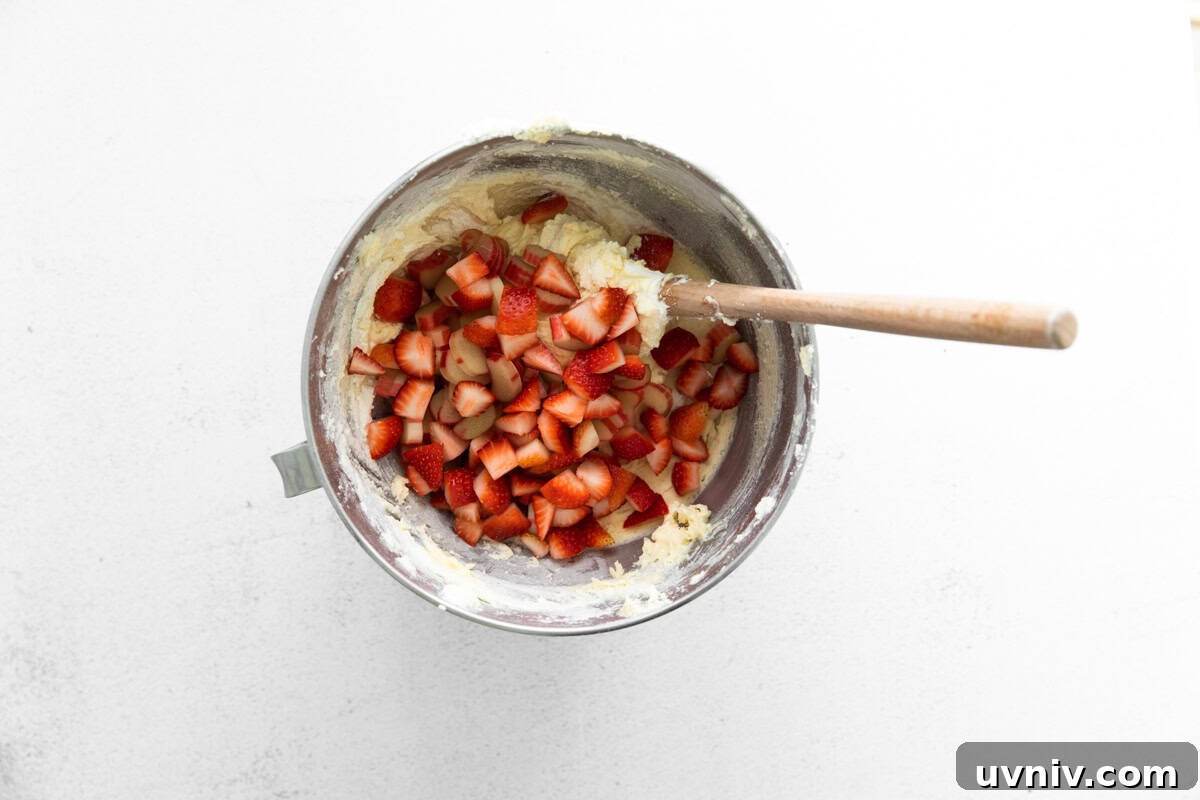 Strawberry Rhubarb Layer Cake Recipe for Summer Baking 8 folding chopped strawberries and rhubarb into cake batter with a rubber spatula.