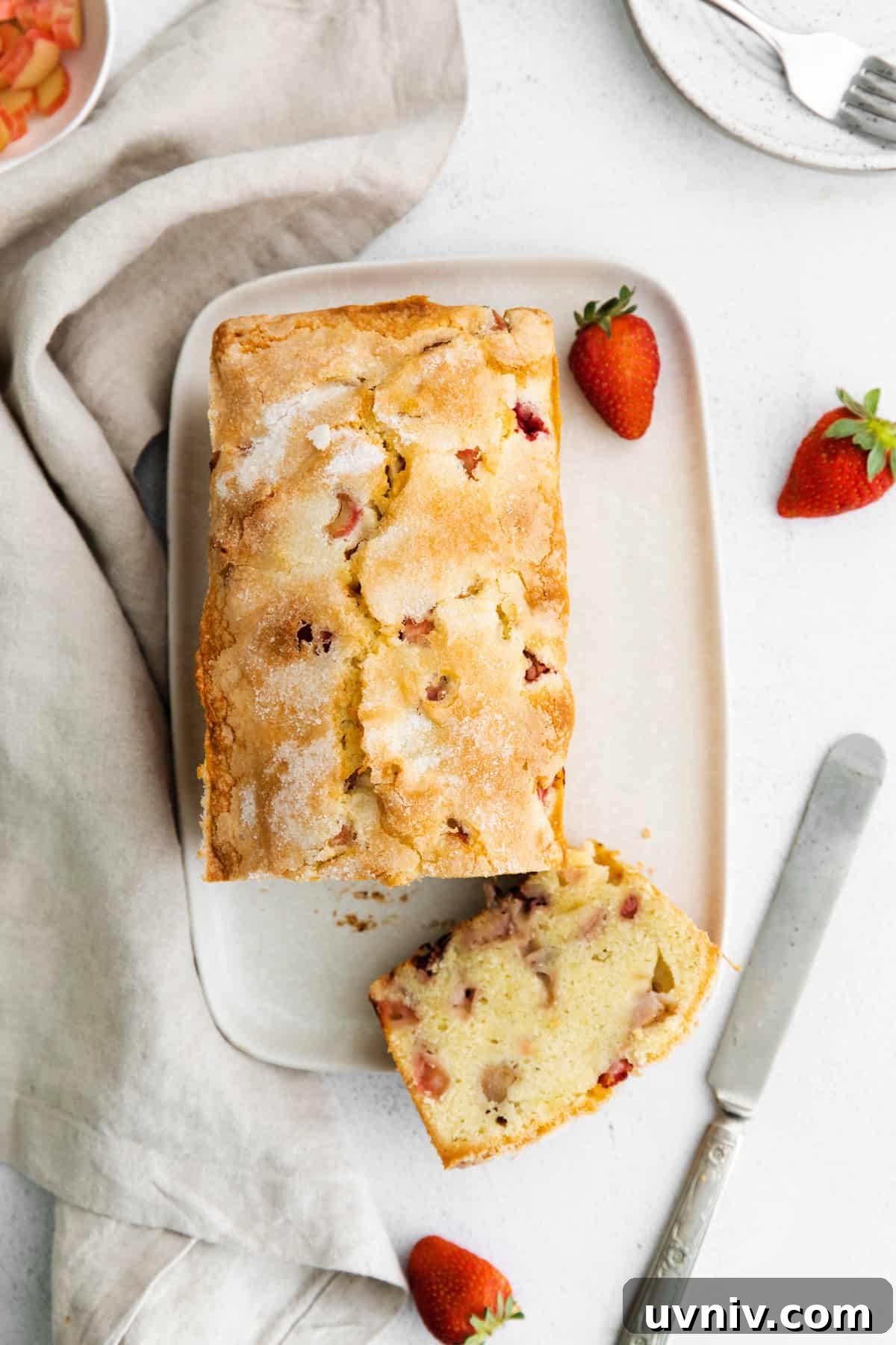 Strawberry Rhubarb Layer Cake Recipe for Summer Baking 3 overhead view of a strawberry rhubarb loaf cake on a rectangular plate with a slice upturned.