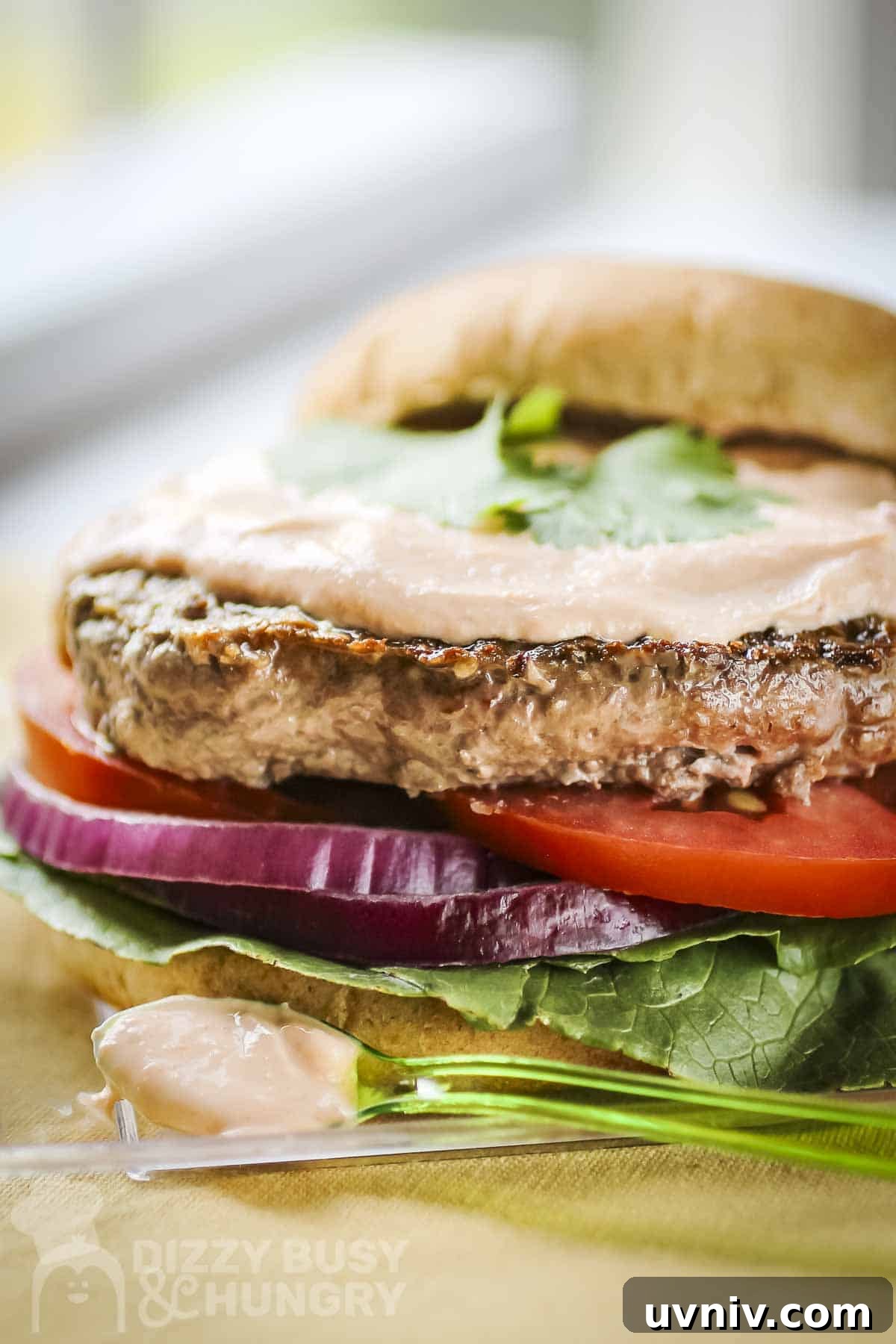 Creamy Sriracha Sauce Recipe for Burgers, Wraps & Sandwiches 2 Side close up shot of a burger assembled with sriracha sauce on top without the top bun on a clear plate.