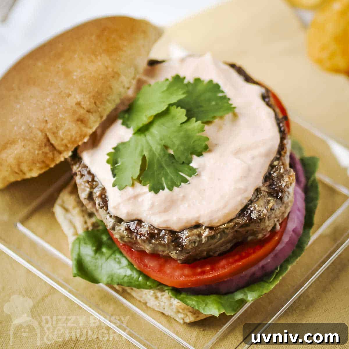 Creamy Sriracha Sauce Recipe for Burgers, Wraps & Sandwiches 7 Overhead shot of a burger with the top bun on the side topped with sriracha sauce on a clear square plate.