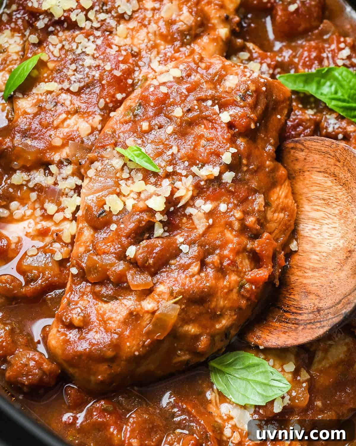 Slow Cooker Italian Chicken Recipe for Tender, Flavorful Meals 13 a wooding spoon under a Slow Cooker Italian Chicken breast in the crockpot garnished with basil and parmesan cheese
