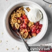 A bowl of strawberry apple crisp with a scoop of vanilla ice cream.