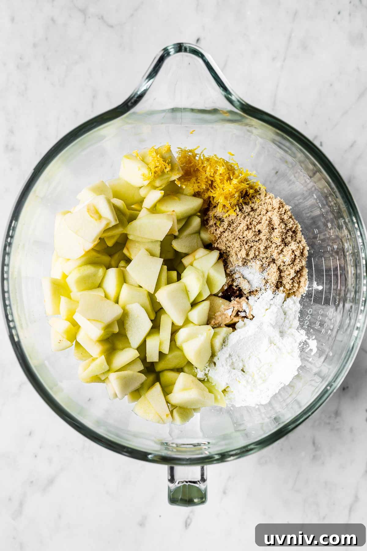 A mixing bowl of apples, lemon zest, sugar and cornstarch.