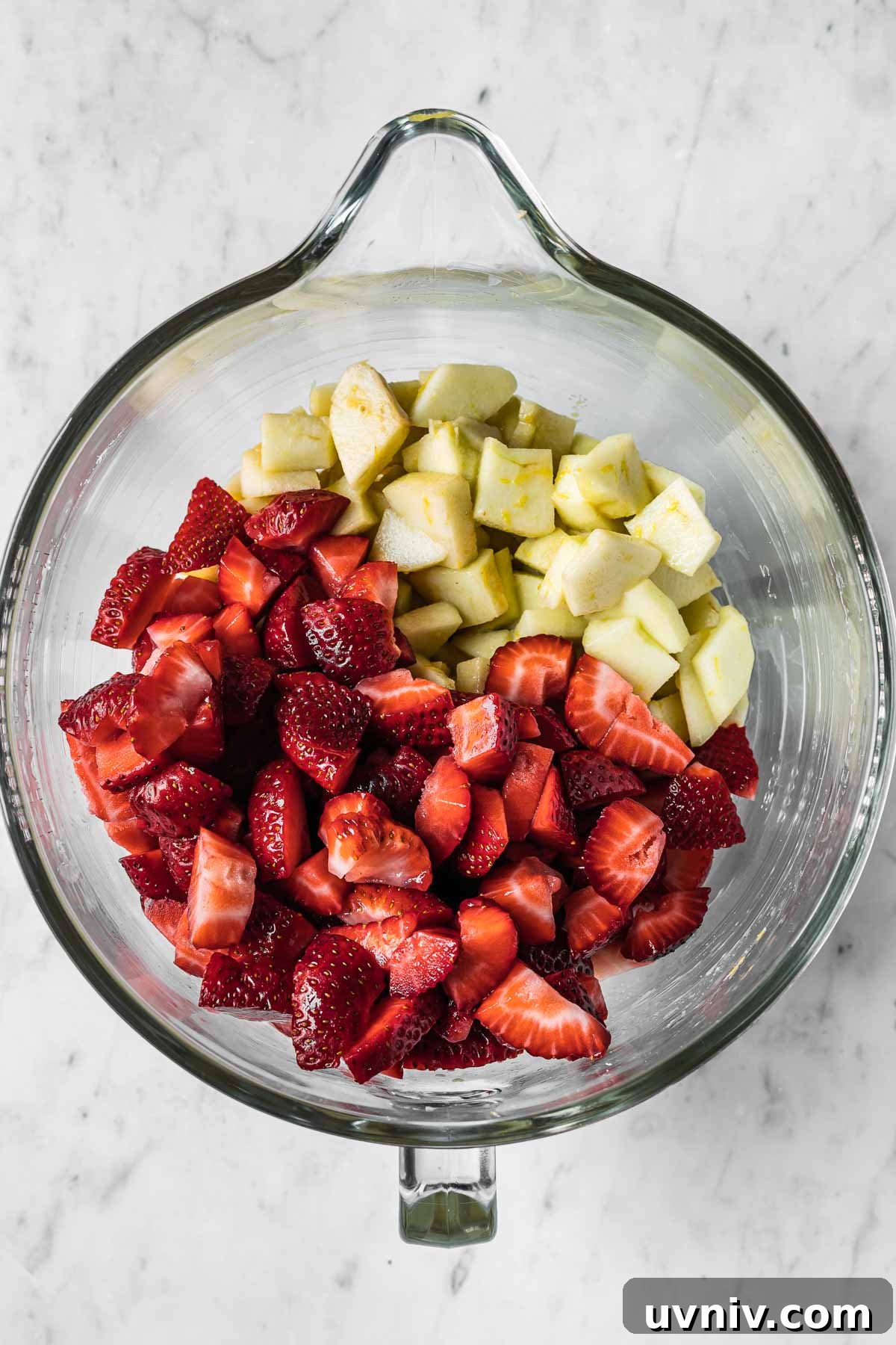 A mixing bowl filled with apples and strawberries for a fruit crisp.