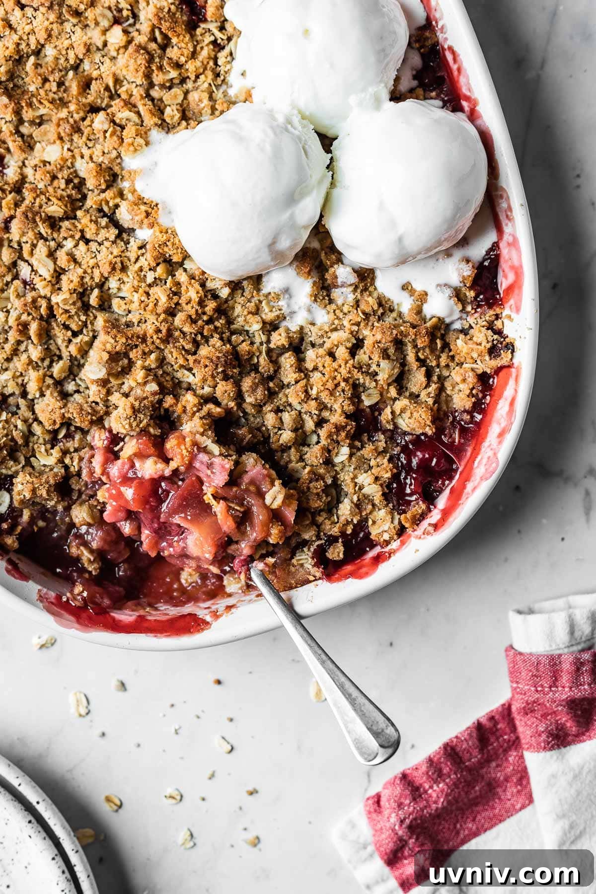 A baked strawberry apple crisp with three scoops of ice cream on top.