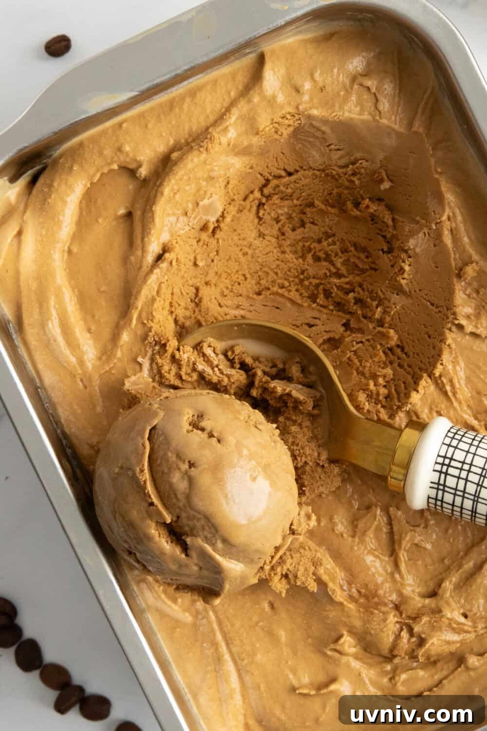 Homemade Espresso Ice Cream Recipe — Rich Coffee Gelato 2 A pan of espresso coffee ice cream being scooped by an ice cream scooper. Espresso beans are in the background.