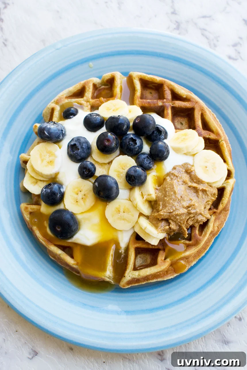 Banana Bread Waffles That Transform Your Weekend Brunch 5 An overhead photo of a round waffle topped with yogurt, bananas, blueberries and peanut butter